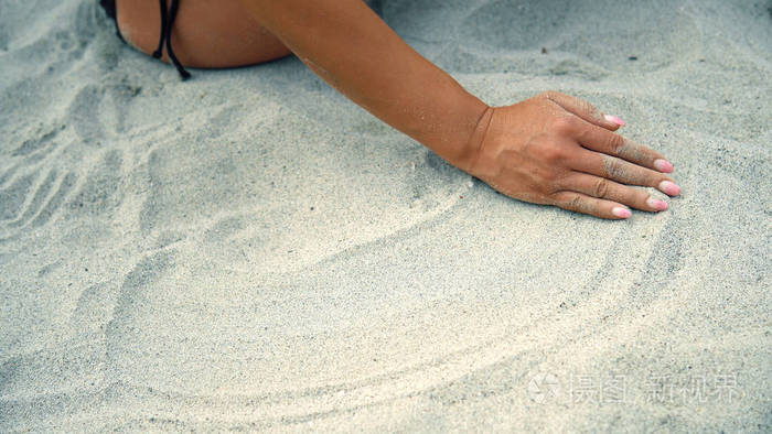 的女人坐在沙滩上，沙子穿过手指