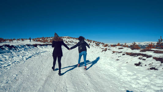两名少女手持双手在雪地上行走,微笑着谈论智能手机照片