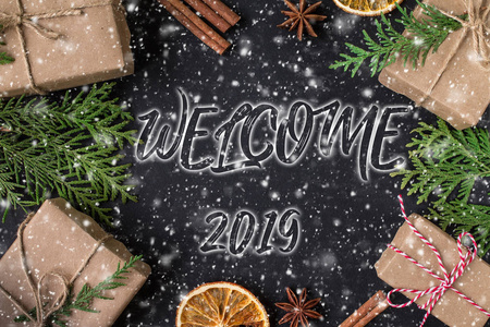欢迎2019年黑色背景上的手写铭文。 松树枝和圆锥形框架。 圣诞贺卡。 寒假作文。 新年和圣诞节庆祝。