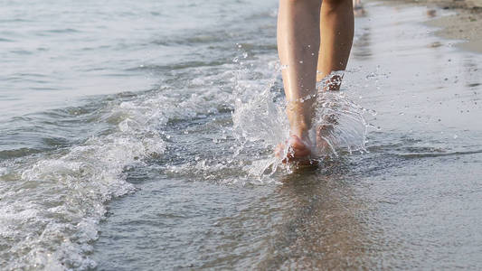 在海上行走的女性赤脚腿的特写镜头被海浪拍击
