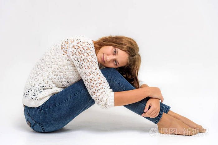 一个年轻漂亮的女孩坐在地板上的白色背景上的肖像.