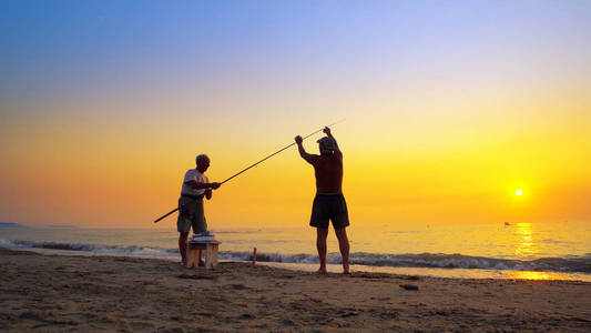 在夏海日落时用鱼竿鱼竿捕鱼的剪影