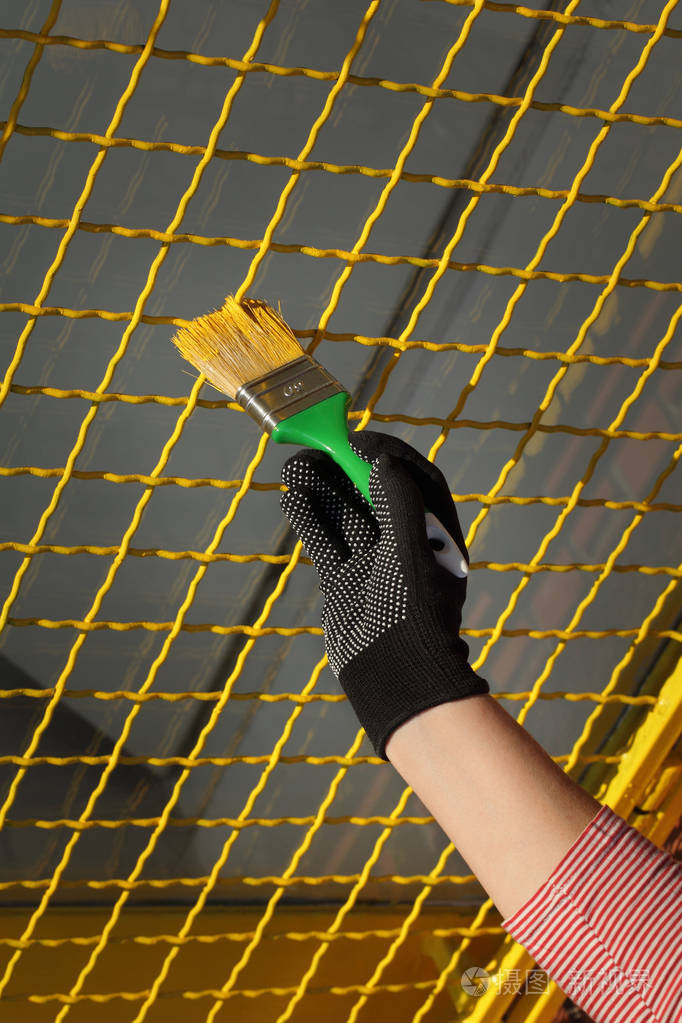 用油漆刷将工人手中的手套漆成金属安全窗网,涂成黄色