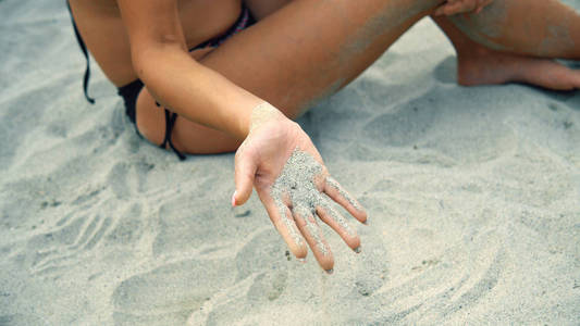 的女人坐在沙滩上，沙子穿过手指
