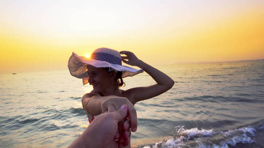 日落时度蜜月的浪漫夫妇。 微笑的女朋友带着帽子，牵着男朋友的手在海滩上散步。 一对夫妇在海滩上享受暑假