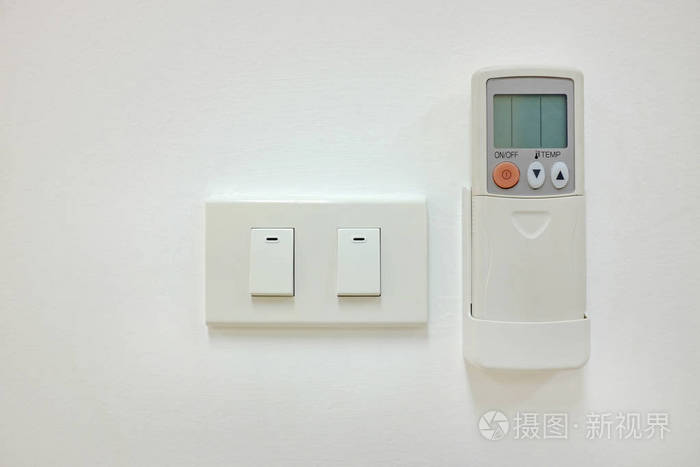 白色墙壁上的电动开关和空调遥控器。