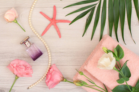一叠柔软的特里毛巾，粉红色的花朵，瓶香水，海星和绿叶在木制背景上。 水疗产品。 上面的风景。