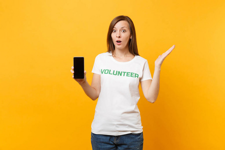 女人穿着白色T恤，写下绿色标题，志愿者拿着手机，空白的空屏隔离在黄色背景上。 自愿无偿援助慈善恩典工作概念