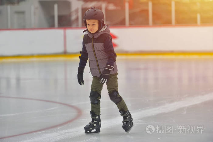 可爱的小男孩穿着冬天的衣服在溜冰场上滑冰