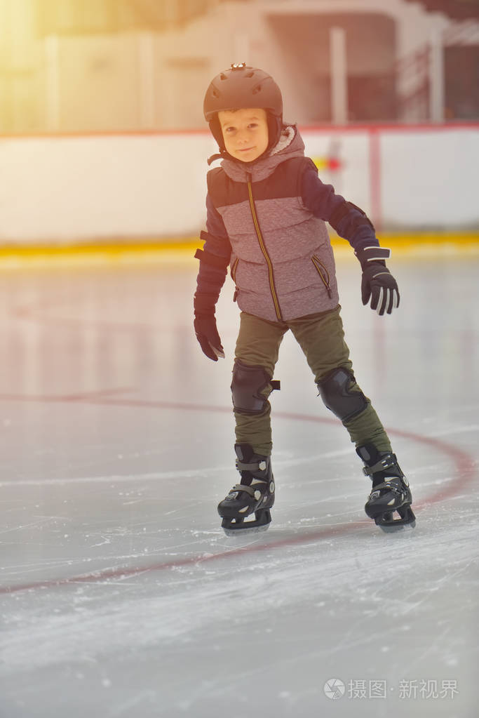 可爱的小男孩穿着冬天的衣服,在溜冰场上滑冰