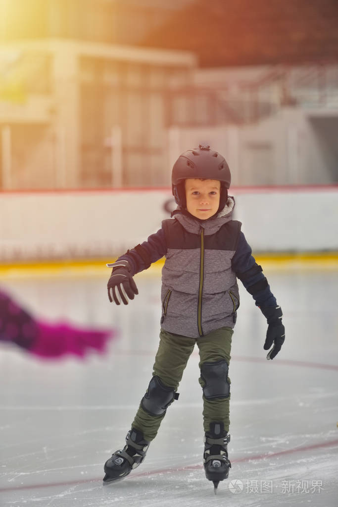 可爱的小男孩穿着冬天的衣服,在溜冰场上滑冰
