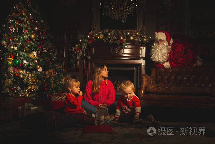 孩子们在圣诞树附近玩耍。 真正的圣诞老人正在看着他们。 庆祝和魔法的气氛。