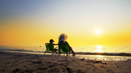 快乐的家庭母子带着帽子在暑假期间在海滩上享受豪华的日落。 旅行概念