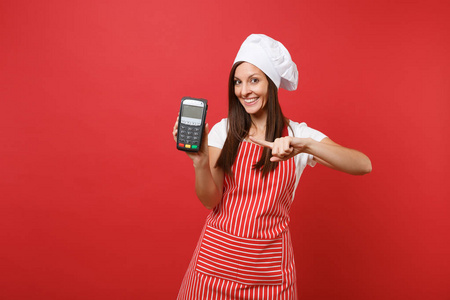 家庭主妇，女厨师或面包师，穿条纹围裙，T恤，厨师帽子，隔离在红墙背景。 女性手持无线银行支付终端NFC设备。 模拟复制空间概念