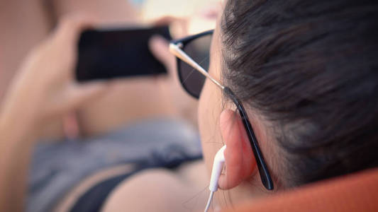 躺在沙滩床上的女青少年在智能手机上听音乐