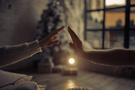在圣诞树灯光和窗户的背景下，男女手互相触摸。