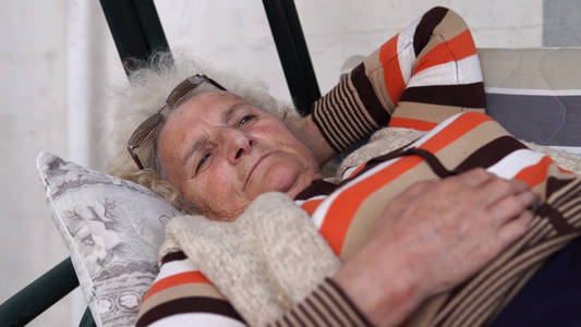 年长的女人微笑着躺在门廊秋千上放松。 电影浅道夫