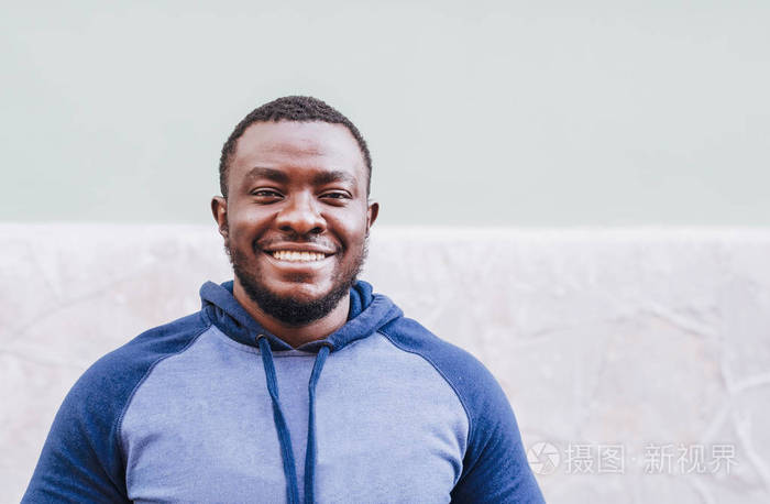 一个开朗,积极的黑人男人的肖像贴在一件运动毛衣上,背景是浅色的墙壁