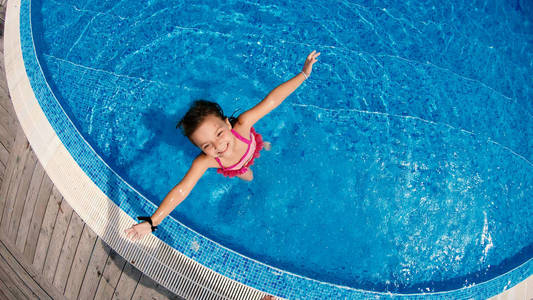 小女孩玩得开心，站在游泳池里，溅上照相机的慢镜头鸟瞰图