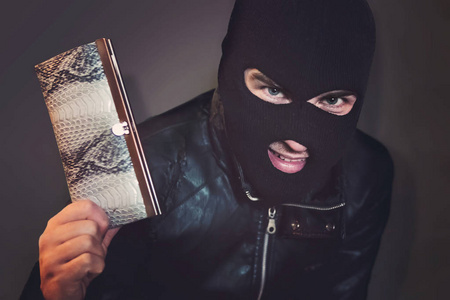 钱包抢夺者蒙面罪犯在黑色的背景下咕哝着看着观众,并显示一个钱包在