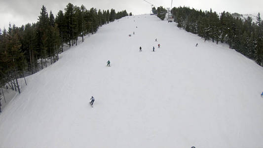 滑雪者和滑雪者在滑雪场的山坡上下山，滑雪场上有雪林滑雪电梯，背景是晴朗的天空下有山，慢动作