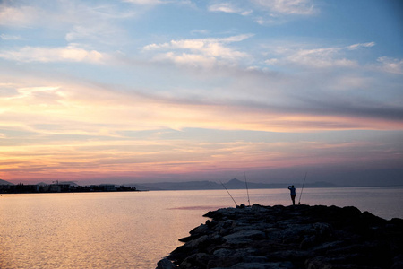 渔人站在码头日落的天空背景，海和山的背景。