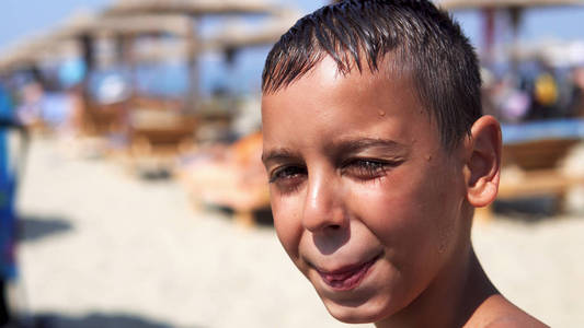 海滩上英俊的男孩看着相机微笑，孩子被夏日的阳光和电影所迷惑