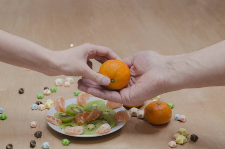女人的手把橘子递给男人，盘子里放着水果，放在桌子的背景下，靠近