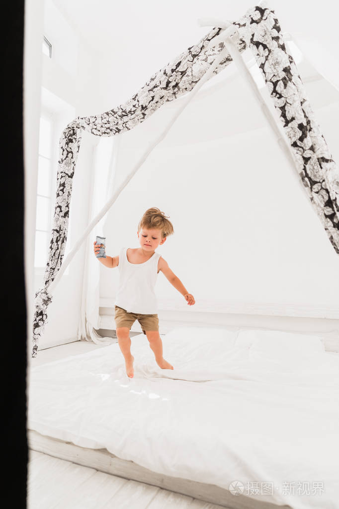 快乐的小男孩在室内的床上蹦蹦跳跳地往下看