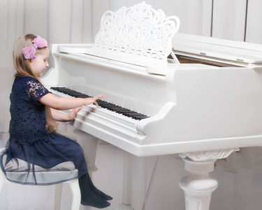 一个漂亮的小女孩正在用一架白色的大钢琴演奏。 儿童音乐和审美教育的概念。