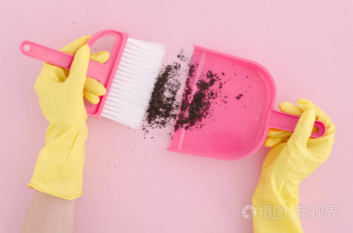 平躺在女性手在黄色乳胶手套收集污垢与刷子和灰尘在粉红色的背景。复制空间。顶部视图。模拟一下