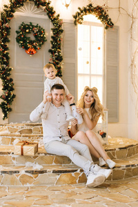 幸福的年轻家庭坐在装饰圣诞节的房子的门廊上。 笑着准备假期