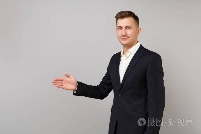 侧面观看英俊的年轻商人,穿着经典西装,站在伸出的手,在灰色的墙壁
