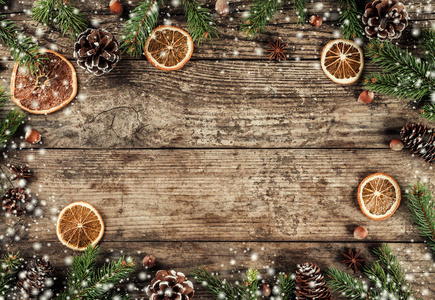 创意布局框架由圣诞杉树枝，云杉片，橙色松果，雪花在木制背景上。 圣诞节和新年主题。 平躺式顶部视图