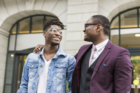 两个年轻而时尚的非洲裔美国人在城市里微笑着说话。父亲和成年儿子关系