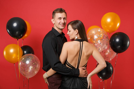 时髦的年轻夫妇穿着黑色衣服庆祝生日，在鲜红的背景气球上举行节日聚会。 圣瓦伦丁国际妇女节2019年新年快乐概念。 嘲弄