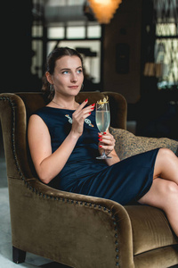 时尚华丽的女孩在一个深蓝色的礼服喝鸡尾酒在豪华的酒店大堂酒吧