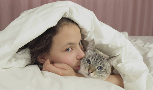 愉快的少女亲吻和谈话与泰国猫在床上