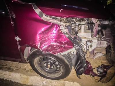 红色新车前面在晚上意外扭曲。 坠毁的新红车严重损坏，需要帮助移动到车库修理和呼叫损失调整器的汽车保险索赔。