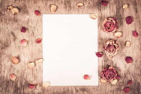空纸和干玫瑰. 木制背景上的空白纸条. 干燥的玫瑰和花瓣. 复制空间.