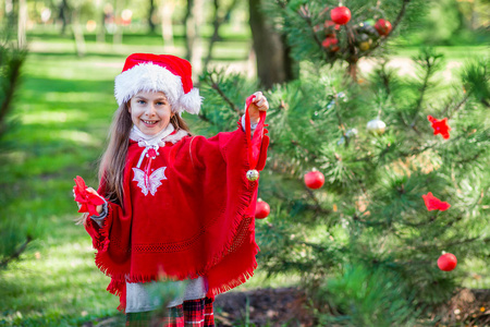 可爱的女孩在假期前在院子里户外装饰圣诞树。 圣诞快乐，节日快乐。