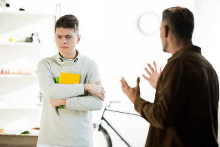 愤怒的父亲打手势，看着悲伤的十几岁的儿子在家