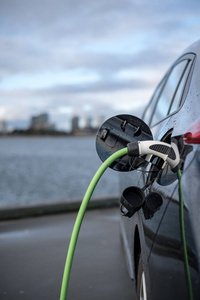 为电动车充电, 背景是城市和水, 绿色充电电缆和黑色汽车。哥本哈根