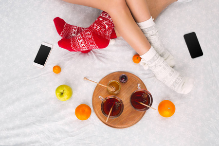软照片的女人和男人在床上与手机和水果, 顶部的观点点。穿着温暖羊毛袜子的女性和男性腿