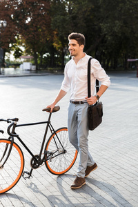 快乐的商人穿着衬衫，骑着自行车在街上散步，背着一个包
