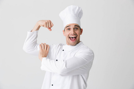英俊兴奋的年轻人厨师形象在室内隔离在白色墙壁背景上，显示二头肌。