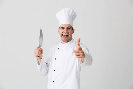 情绪激动的年轻男子厨师在室内被隔离在白色墙壁背景上,手持刀指着