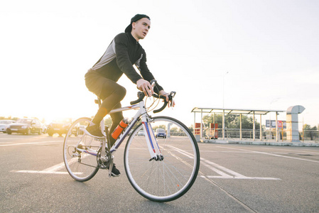 一个迷人的骑自行车的人在运动的肖像。骑着黑色自行车的年轻人在街上骑着自行车，夕阳下晒着太阳。