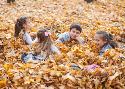 孩子们在秋天的城市公园里躺在落叶上玩耍。