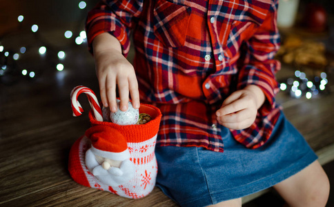 一个穿着格子红色衬衫的孩子从一份甜蜜的圣诞礼物中取出糖果。 圣诞节早晨的概念。 快关门。 选择性聚焦。